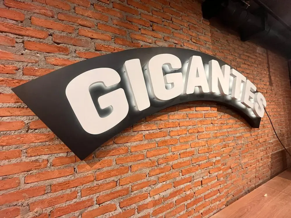 Gigantes — letreiro curvo iluminado em parede de tijolos